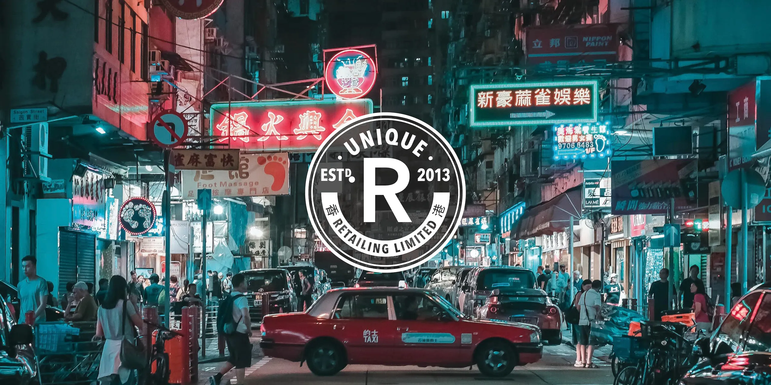 Unique Retailing rondel logo in white on a background of a neon lit Hong Kong street at night with a red taxi crossing to the right.